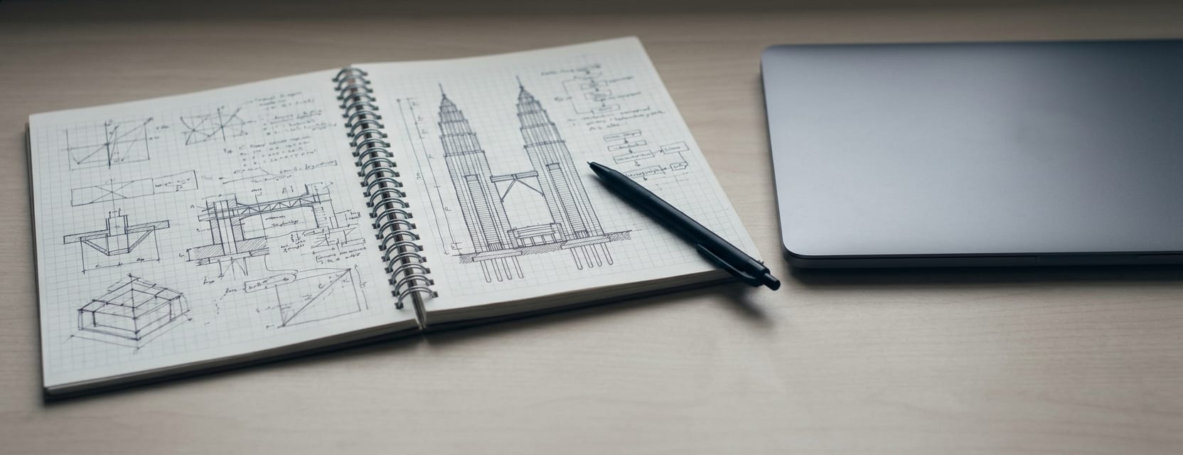 A notebook of system sketches open beside a closed laptop.